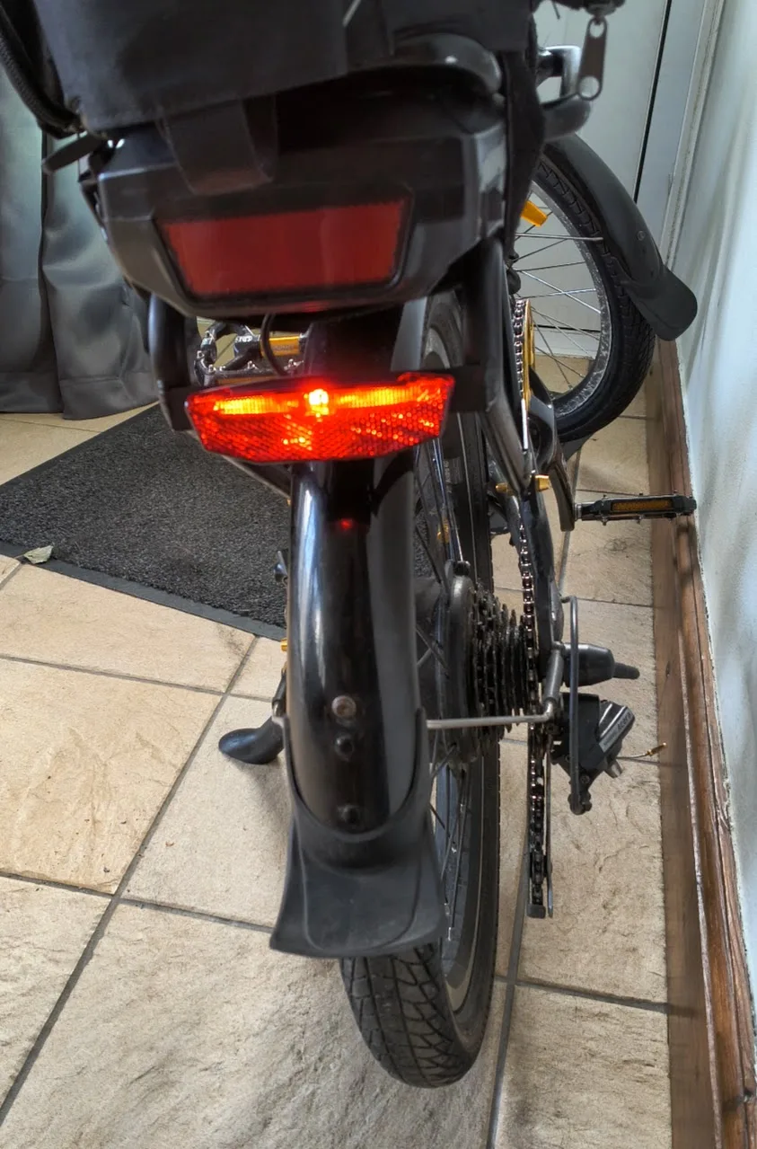 The new rear light fitted and lit, glowing red, mounted low on the rear mudguard stay
